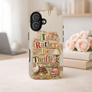 Peut inclure: Une coque de téléphone beige avec un design en collage portant le texte I'd Rather Be Thrifting. Le graphique comprend une oie blanche, une pile de livres anciens, une lampe, une carafe florale, des tasses et une étiquette de prix de 25 cents.