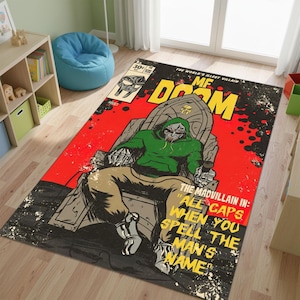 以下が含まれることがあります： MF DOOMのコミック風イラストが描かれた長方形のラグ。デザインには赤い背景、「MF DOOM」の文字、「THE MADVILLAIN IN: ALL CAPS WHEN YOU SPELL THE MAN'S NAME」のテキストが含まれています。キャラクターは緑色のパーカーを着ています。