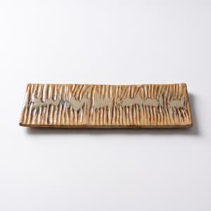 Puede incluir: Una fuente rectangular de cerámica con superficie texturizada. La fuente es de color beige claro con ranuras verticales y un borde ligeramente elevado. El diseño tiene una estética rústica y artesanal.