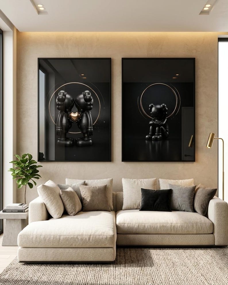May include: Two framed wall art prints featuring black cartoon-style figures with X-shaped eyes. The left print shows two figures touching heads with a gold heart between them, while the right print shows a single figure sitting with knees pulled up.