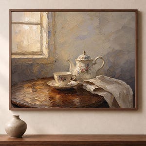 Puede incluir: Una pintura al óleo en un marco marrón que representa un bodegón sobre una mesa redonda de madera. Una tetera de porcelana blanca y una taza a juego sobre un platillo están colocadas junto a un paño blanco doblado, con una ventana al fondo.