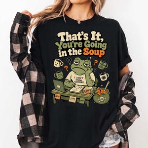 Peut inclure: T-shirt noir avec l'inscription "That's It, You're Going in the Soup". Le motif présente une grenouille de dessin animé avec une expression stressée, entourée de points d'interrogation et de tasses à café. La grenouille porte un t-shirt avec l'inscription "I Don't Know Anymore."