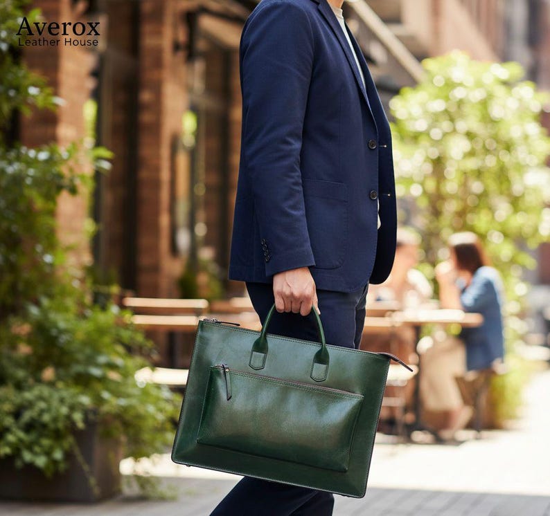 Pode incluir: Uma pasta de couro verde com um bolso frontal a condizer e al&ccedil;as superiores &eacute; transportada por uma pessoa que usa um fato azul marinho. A pasta tem um acabamento brilhante. A marca "Averox Leather House" &eacute; vis&iacute;vel no canto superior esquerdo.