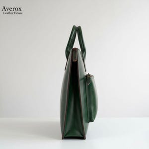 Pode incluir: Uma mala tote de couro verde escuro com um pequeno bolso preso. A mala tem uma forma estruturada com uma al&ccedil;a na parte superior. A mala &eacute; feita de couro e tem um design minimalista. A mala &eacute; adequada para transportar itens do dia a dia.