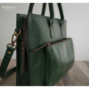 Pode incluir: Uma pasta de couro verde com uma al&ccedil;a de ombro e al&ccedil;as superiores. A bolsa tem um bolso frontal com z&iacute;per e um z&iacute;per para o compartimento principal. O hardware &eacute; de cor lat&atilde;o. A marca "Averox Leather House" est&aacute; impressa no canto superior esquerdo.
