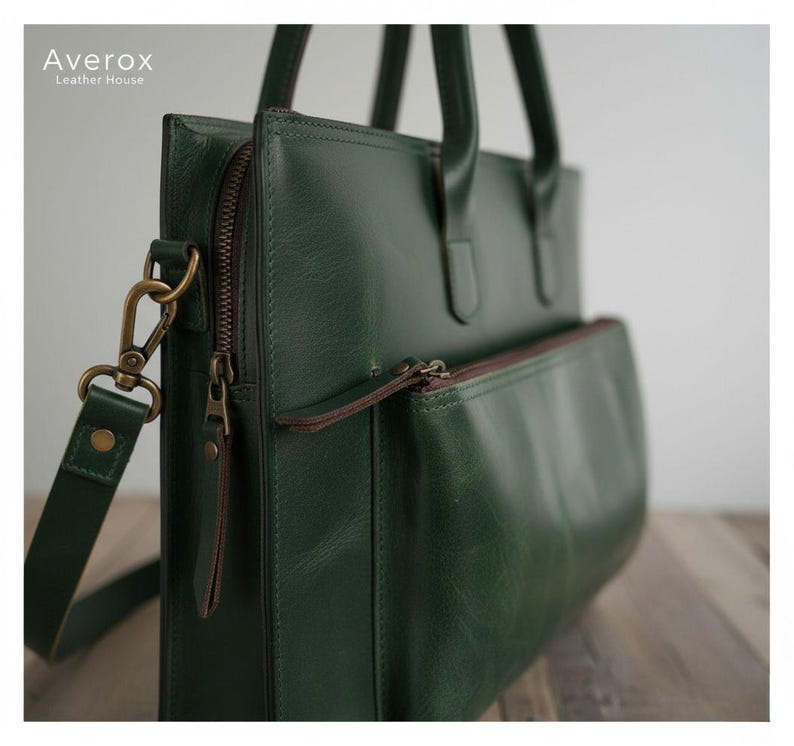 Pode incluir: Uma pasta de couro verde com uma al&ccedil;a de ombro e al&ccedil;as superiores. A bolsa tem um bolso frontal com z&iacute;per e um z&iacute;per para o compartimento principal. O hardware &eacute; de cor lat&atilde;o. A marca "Averox Leather House" est&aacute; impressa no canto superior esquerdo.