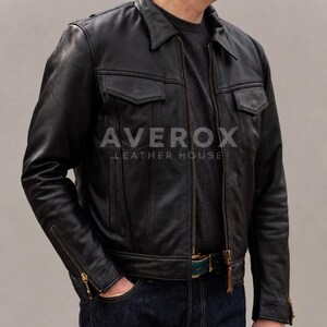 Op de afbeelding: Een zwart leren jack met een puntige kraag, een ritssluiting over de hele lengte, twee borstzakken met kleppen en manchetten met rits. De tekst AVEROX LEATHER HOUSE is in het wit gedrukt op het borstgedeelte van het jack.
