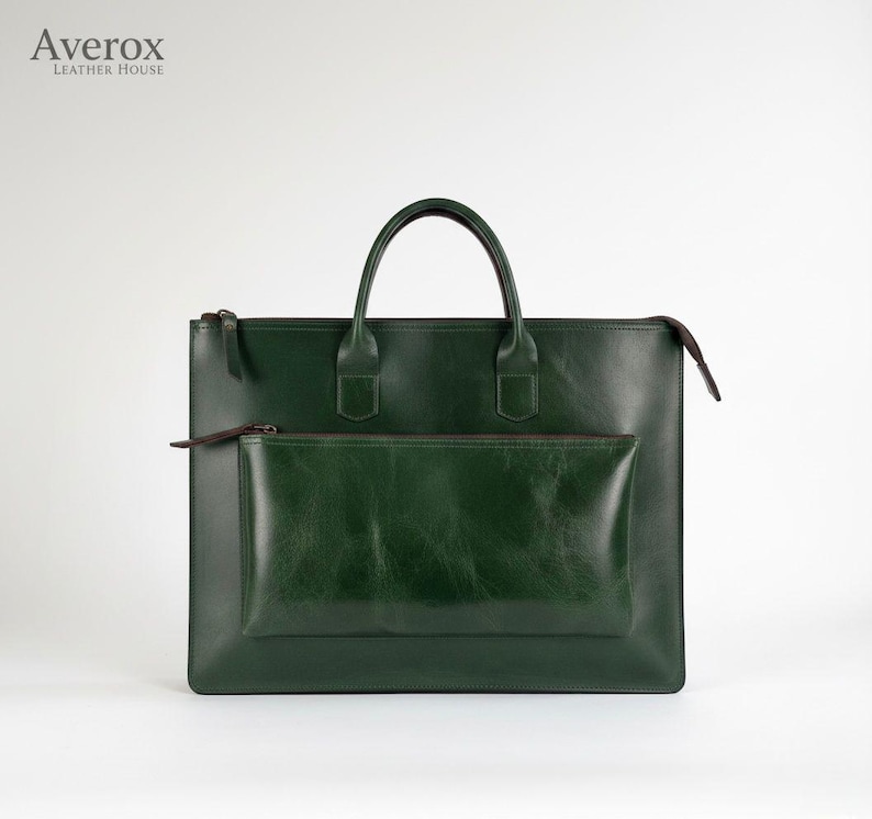 Pode incluir: Uma pasta de couro verde escuro com uma al&ccedil;a superior e um bolso frontal. A bolsa tem fecho de z&iacute;per e um design minimalista. A marca "Averox Leather House" est&aacute; no canto superior esquerdo.