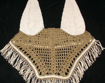 May include: A tan and cream-colored crochet horse bonnet with ear covers. The bonnet features a detailed openwork design with a cream-colored border and fringe along the bottom edge. The ear covers are a solid cream color.