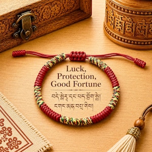 May include: A red, yellow, and green braided cord bracelet with an adjustable sliding knot closure. The centre features the text Luck, Protection, Good Fortune, followed by two lines of Tibetan script printed on the surface inside the bracelet.