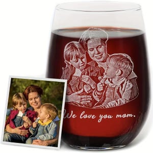 May include: A clear stemless wine glass filled with dark red liquid, featuring a white laser-etched engraving of a woman and two children. Below the etched figures, the text "We love you mom." is engraved in a white cursive script font.