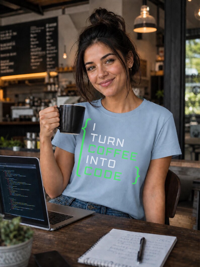 May include: A light blue short-sleeve t-shirt featuring the text "I TURN COFFEE INTO CODE" in white and green lettering, framed by green curly brackets. The shirt is made of a soft fabric and has a crew neckline, providing a casual look.
