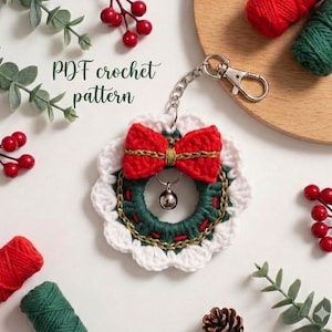 May include: A handmade crochet Christmas wreath keychain with a red bow, green wreath, and silver bell. The keychain is attached to a silver chain and clasp. The text "PDF crochet pattern" is visible.