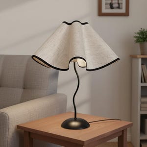 May include: A table lamp featuring a wavy, beige fabric lampshade with a thin black trim along the edges. The lamp has a slender, curved black metal stem that connects to a smooth, circular black base, providing a stable foundation for the light.