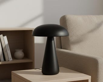 May include: A black mushroom-shaped table lamp with a rounded top and a conical base. The lamp is made of a matte black material and sits on a light-colored wooden side table. The lamp is plugged into an electrical outlet.