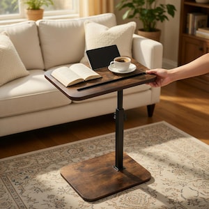 May include: A height-adjustable side table with a dark brown wood-grain finish and a black metal support column. The rectangular tabletop features a built-in slot, holding an open book, a black tablet, and a white ceramic coffee cup on a saucer.