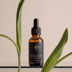 May include: A brown glass bottle with a black dropper and a black label. The label reads "MOON SISTER" and "RADIANCE RENEWING OIL SERUM". The bottle is 1 fl oz (30 ml). Green leaves frame the bottle against a neutral background.