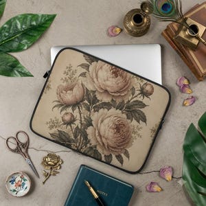 Op de afbeelding: Een rechthoekige laptophoes met een beige achtergrond en een gedetailleerde botanische illustratie van bloeiende pioenrozen en knoppen in gedempte bruin- en crèmetinten, afgewerkt met een zwarte ritssluiting en zachte beschermende stof.