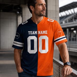May include: A split-color jersey featuring a dark navy blue right side and a bright orange left side. The chest displays the text "TEAM NAME" above the large white number "00". The sleeves have white and navy stripes, with "logo" text.