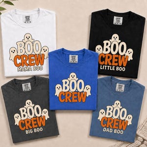 May include: Five t-shirts in white, black, dark grey, blue, and light blue. Each shirt features a graphic of three ghosts above the text BOO CREW in orange. Specific shirts include the additional text MAMA BOO, LITTLE BOO, BIG BOO, or DAD BOO.