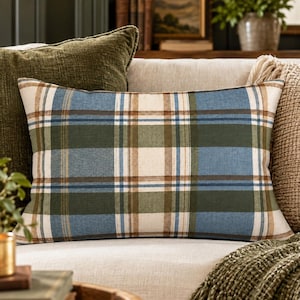 May include: A rectangular throw pillow featuring a plaid pattern in shades of muted blue, forest green, cream, and brown. The fabric displays a classic intersecting grid design with horizontal and vertical stripes of varying widths and colors.