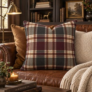 May include: A square scatter cushion featuring a plaid pattern in shades of deep burgundy, forest green, and cream. The fabric has a soft texture, and the cushion is plumply filled, displaying a classic grid design with intersecting horizontal and vertical lines.