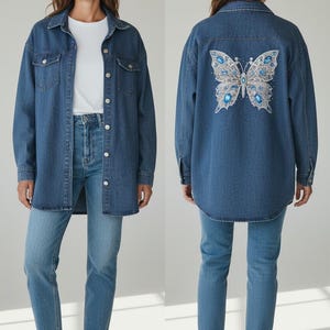 May include: A blue denim shirt jacket featuring a classic collar, long sleeves, and silver-tone metal buttons. The back displays a large, detailed butterfly embroidery in shades of blue, silver, and white, accented with sparkling blue rhinestones.