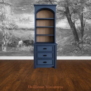 May include: A navy blue miniature cabinet with three drawers and open shelving. The cabinet has an arched top with vertical wooden slats. The background features a black and white landscape painting. The text "Dollhouse Miniatures" is at the bottom.