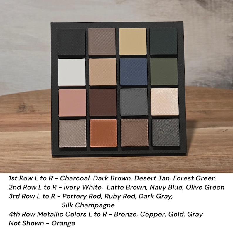 May include: A black square display board with sixteen color swatches arranged in four rows. Colors include charcoal, dark brown, desert tan, forest green, ivory white, latte brown, navy blue, olive green, pottery red, ruby red, dark gray, silk champagne, bronze, copper, gold, and gray.