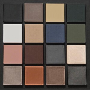May include: A square palette featuring sixteen individual square eyeshadow pans in a variety of colors. The colors include black, brown, beige, white, blue, green, pink, and gray. The pans are arranged in a grid pattern within a black frame.