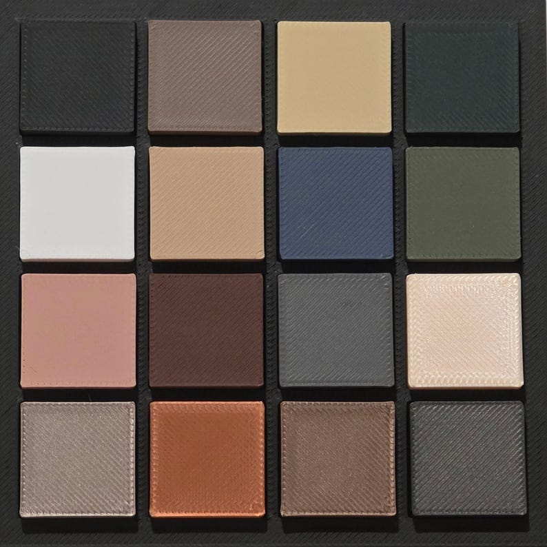 May include: A square palette featuring sixteen individual square eyeshadow pans in a variety of colors. The colors include black, brown, beige, white, blue, green, pink, and gray. The pans are arranged in a grid pattern within a black frame.