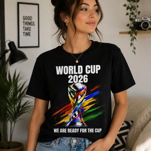 Könnte beinhalten: Schwarzes T-Shirt mit dem Text "WORLD CUP 2026" und einer farbenfrohen Trophik-Grafik. Das Shirt enthält auch den Satz "WE ARE READY FOR THE CUP". Das Design zeigt regenbogenfarbene Pinselstriche.