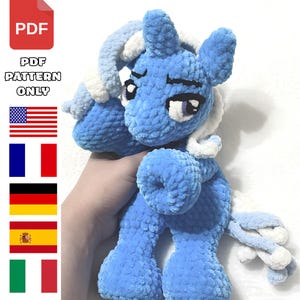 Peut inclure: Une peluche poney crochetée bleue avec une crinière et une queue blanches, dotée de grands yeux sombres et d'une finition en fil texturé doux. L'image inclut une icône PDF rouge et le texte PDF PATTERN ONLY, ainsi que des drapeaux des États-Unis, de France, d'Allemagne, d'Espagne et d'Italie.