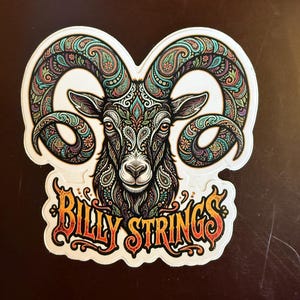 May include: A sticker featuring a detailed illustration of a ram's head with large, curved horns. The ram is adorned with intricate paisley patterns in shades of teal, purple, and orange. The text "Billy Strings" is displayed in a stylized font.