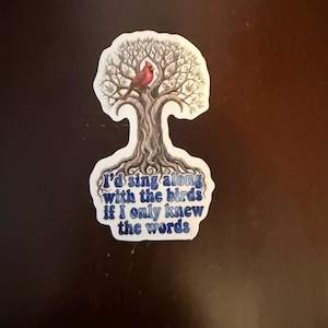 May include: A sticker featuring a tree with a red cardinal perched in its branches. The sticker has the text "I'd sing along with the birds if I only knew the words" in blue script. The sticker is white with a blue border.