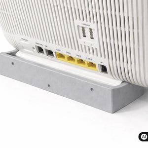 Könnte beinhalten: Ein weißer Internet-Router mit vertikalen Lüftungsschlitzen ist in einem hellgrauen, rechteckigen Kunststoffständer montiert. Die Rückseite verfügt über vier gelbe LAN-Anschlüsse, zwei Telefonanschlüsse mit der Beschriftung 1 und 2 sowie diverse Eingänge.