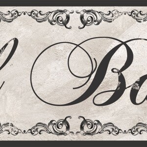 May include: A black and white sign with a decorative border. The sign reads "El Baño" in a cursive font.