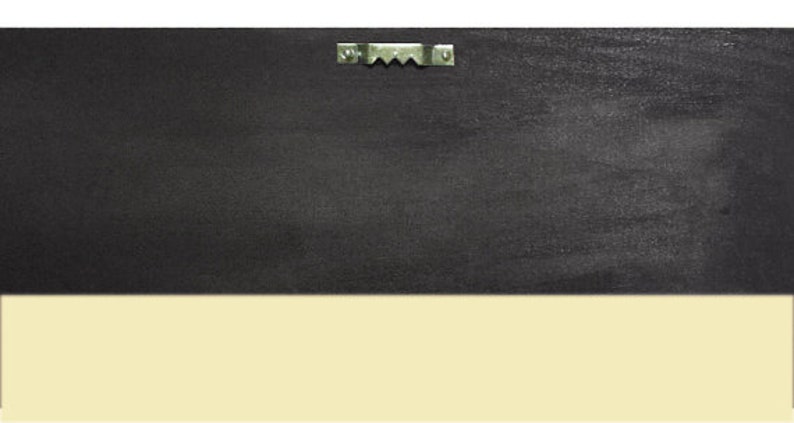May include: The back of a black framed picture with a metal hanging hook.
