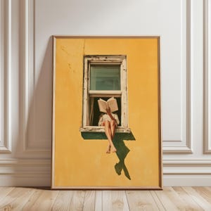 May include: A framed wall art print featuring a bright yellow wall with a single window. A person sits on the window ledge, reading an open book that obscures their face. The person wears light-colored clothing and has bare feet dangling below.