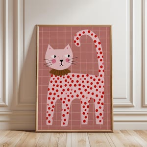 Può includere: Una stampa artistica incorniciata raffigurante un gatto rosa chiaro stilizzato con pois rossi sul corpo e sulla lunga coda. Il gatto indossa un colletto marrone a balze su uno sfondo rosa polvere con un motivo a griglia bianca.