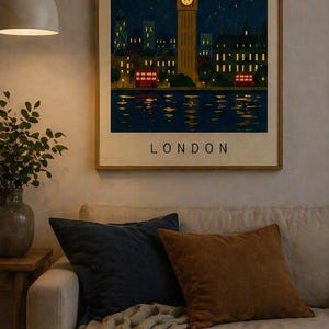 Può includere: Una stampa artistica incorniciata raffigurante Londra di notte, con il Big Ben, autobus rossi a due piani e la scritta "LONDON". La stampa è appesa sopra un divano beige con cuscini blu navy e marroni. Una candela accesa è su un tavolino di legno.