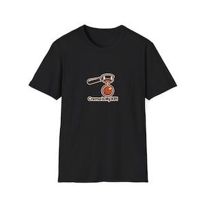 May include: A black short-sleeve t-shirt featuring a graphic of a coffee portafilter pouring espresso into a cup. Below the graphic, the text reads "Crema Is My KPI" in a light-colored, rounded font. The design is centered on the chest area.