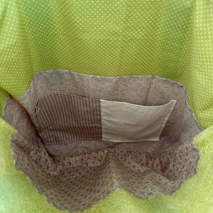 May include: A handmade tote bag with a bright green polka dot exterior and a floral patterned interior. The bag features a brown pocket with a striped and solid fabric design. The handles are a bright blue.