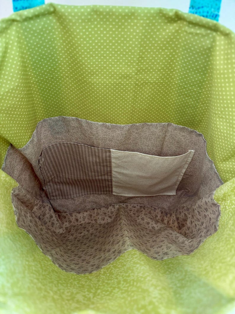May include: A handmade tote bag with a bright green polka dot exterior and a floral patterned interior. The bag features a brown pocket with a striped and solid fabric design. The handles are a bright blue.
