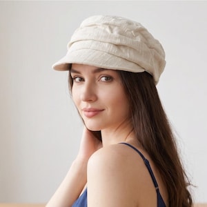 May include: A cream-colored newsboy cap with a textured fabric finish and a short, stiff brim. The hat features a gathered, multi-paneled crown design that sits comfortably on the head, providing a structured yet soft appearance for daily wear.