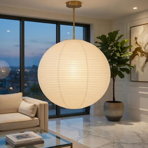 May include: A large, spherical pendant light fixture with a white, ribbed paper shade suspended from a thin, brass-colored metal rod and ceiling mount. The light emits a soft, warm glow, illuminating the textured surface of the paper material.