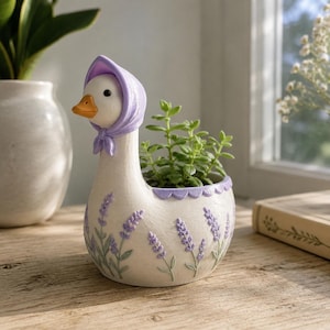 May include: A white goose-shaped planter featuring a lavender-coloured headscarf, an orange beak, and a textured body decorated with painted purple lavender sprigs and green stems. The top edge of the planter has a scalloped purple trim design.