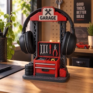 May include: A black and red garage-themed headphone stand featuring a sign that reads GARAGE with a crossed wrench icon. The stand includes a miniature tool chest with visible wrenches, a screwdriver, pliers, a tape measure, and a stack of tires.