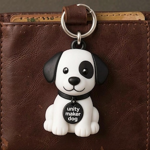 May include: A white and black dog keychain with a black collar and a silver keyring. The dog has a black spot over one eye and black ears. The tag reads "unity maker dog".