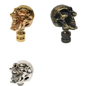 May include: Three skull finials in gold, antique brass, and silver finishes. Each finial features a detailed skull design with a textured surface.